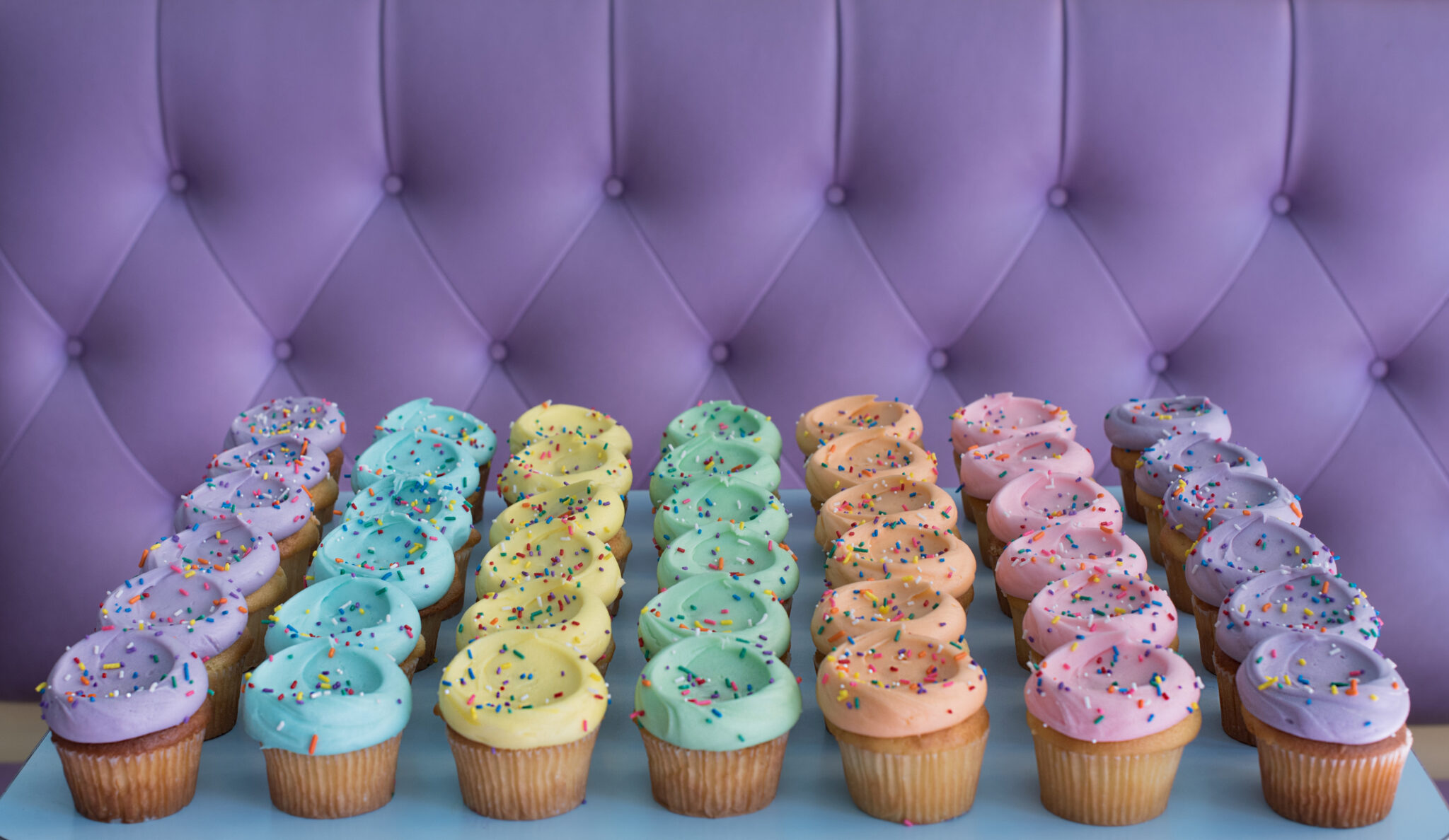 lots of pastel colored cupcakes on a purple couch